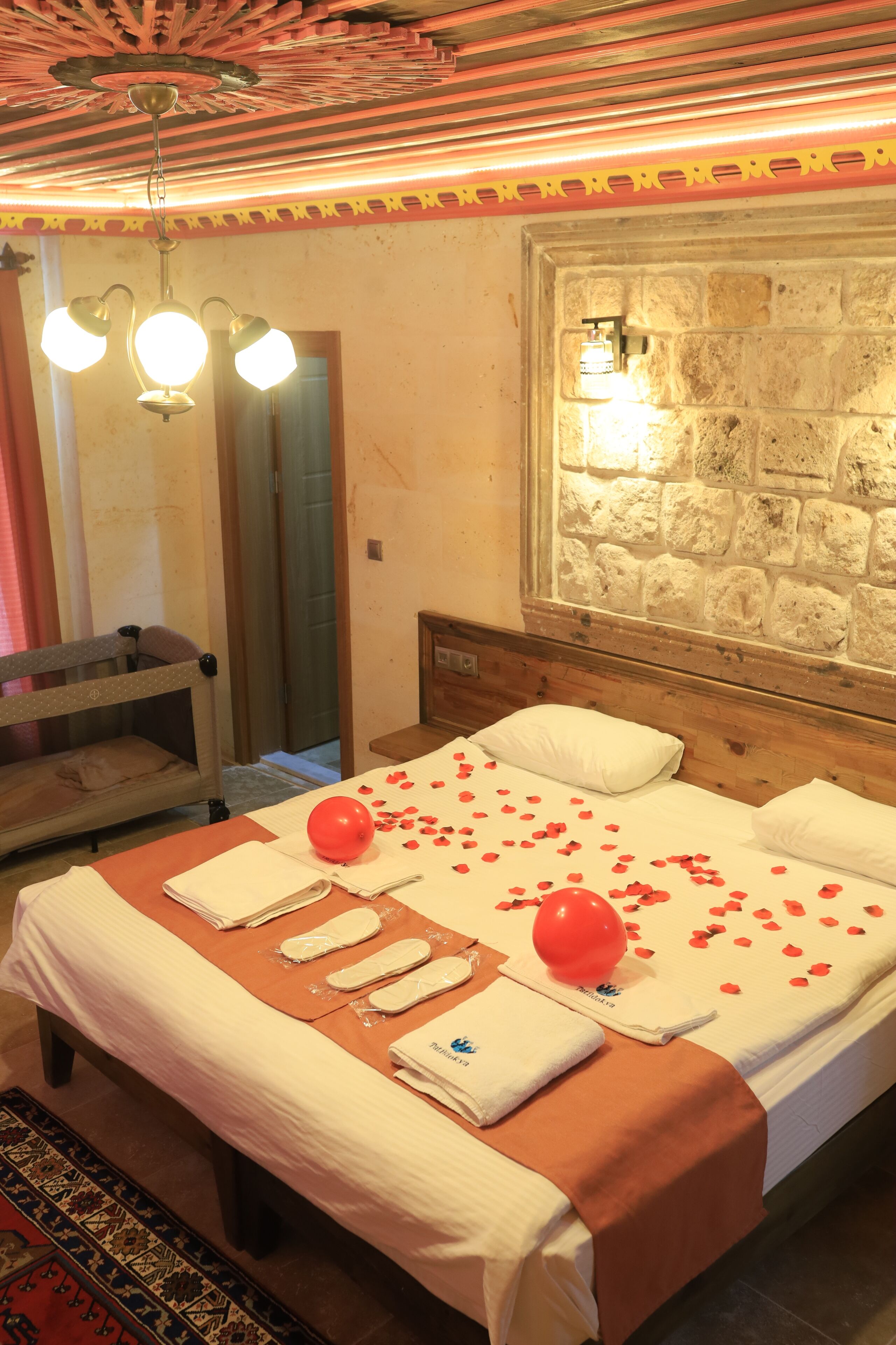 A hotel room with a bed, a wooden headboard, a stone wall, a mirror, and a hanging light fixture.
