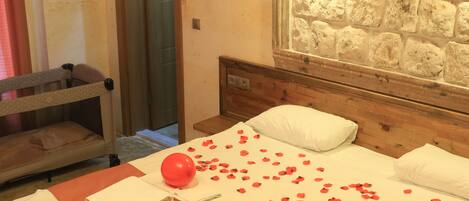 A hotel room with a bed, a wooden headboard, a stone wall, a mirror, and a hanging light fixture.