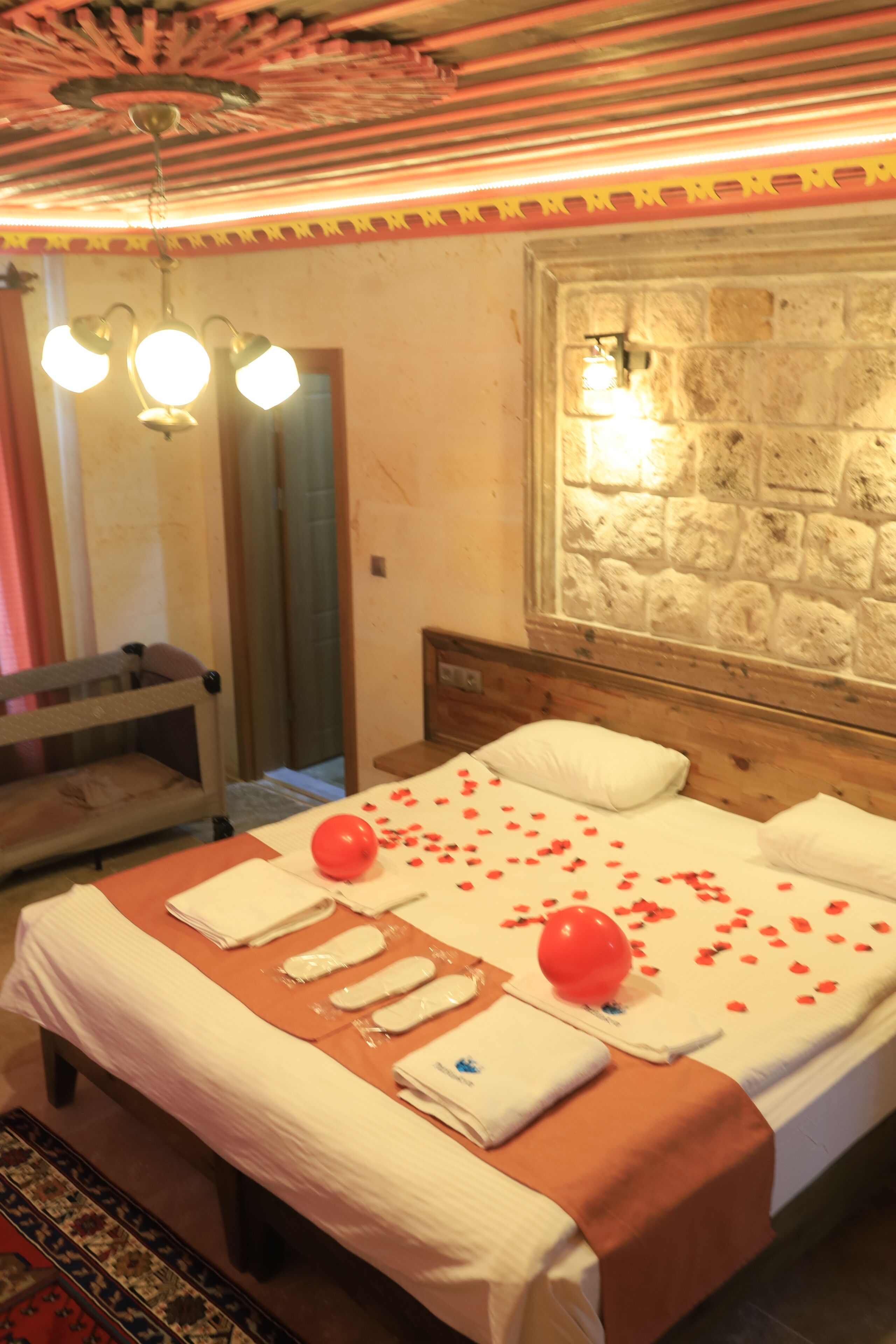 Una habitación de hotel con cama, cabecero de madera, pared de piedra y techo con diseño decorativo.