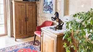 Una stanza con parete in pietra, un armadio in legno, una sedia rossa, una scrivania con una pianta e un televisore fissato alla parete.