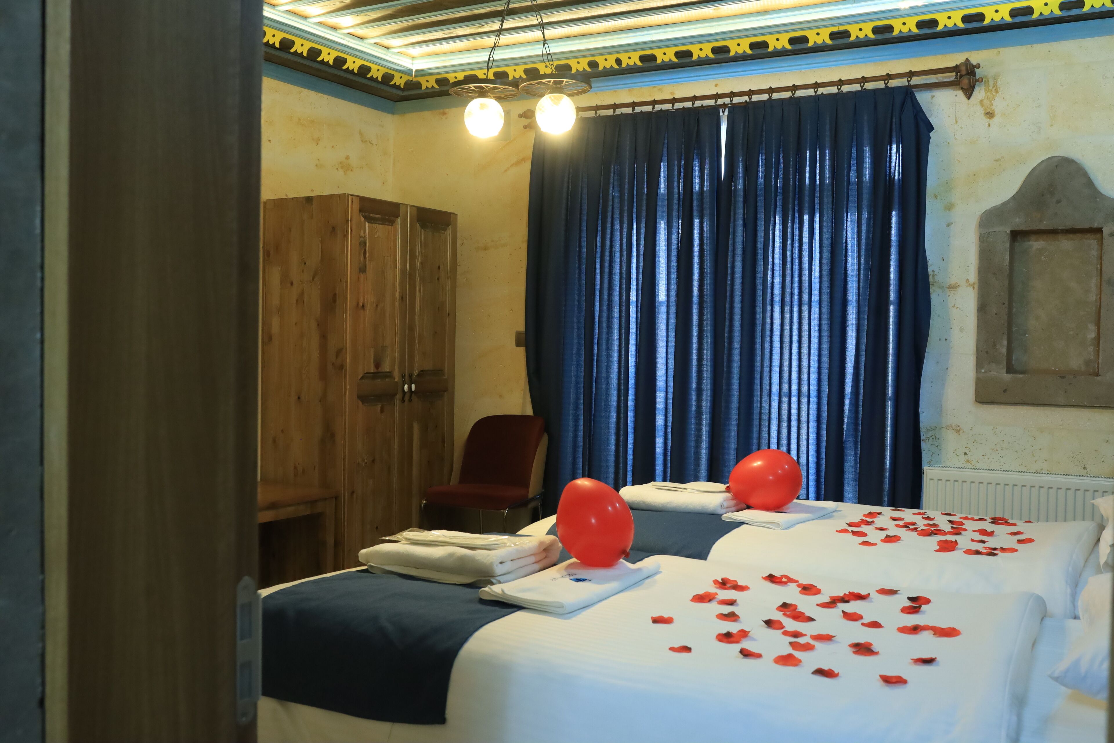 Habitación de hotel con dos camas, un armario de madera, una silla roja y un ventanal con cortinas azules.