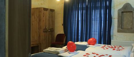 Habitación de hotel con dos camas, un armario de madera, una silla roja y un ventanal con cortinas azules.
