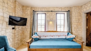 Una stanza con parete in pietra, un letto di legno con biancheria azzurra, una poltrona blu e una TV a schermo piatto montata a parete.