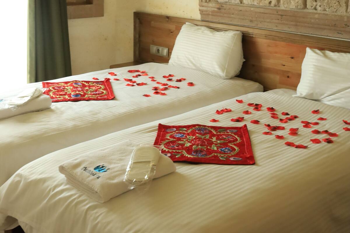 A hotel room with two beds, a stone wall, a wooden headboard, and a green curtain.