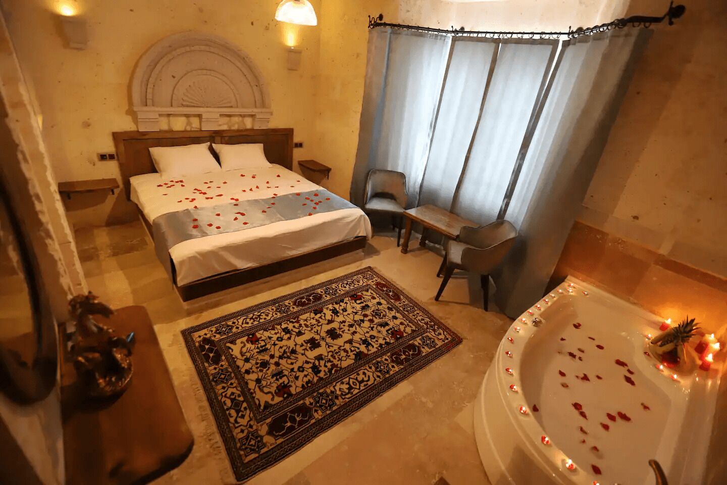 Hotelkamer met twee bedden, een zithoek met een tafel en stoelen, een groot vloerkleed en een badkuip met rozenblaadjes.
