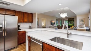 A modern kitchen with a stainless steel refrigerator, wooden cabinets, a white countertop, and a large sink. - Summer Deal Waikoloa Condo Near Beaches with Golf Course Views (Waikoloa)