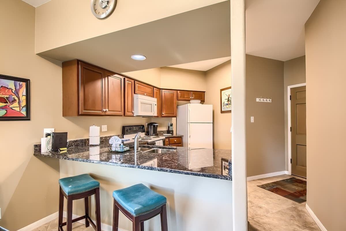 A kitchen with wooden cabinets, a microwave, a refrigerator, a sink, and two bar stools.