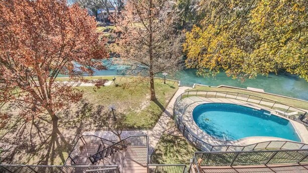 A swimming pool with a surrounding deck, a view of a river, and trees with autumn foliage. - IC 209 Comal Escape (NEW BRAUNFELS)