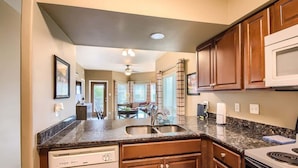 A kitchen with granite countertops, wooden cabinets, a dishwasher, a microwave, and a dining area with a table and chairs. - IC 209 Comal Escape (NEW BRAUNFELS)
