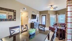 A dining area with a glass table, chairs, and a decorative bowl. There is a sofa and a television in the background. - IC 209 Comal Escape (NEW BRAUNFELS)