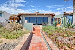 A modern house with a patio, a thatched roof structure, and a pathway leading to the entrance.