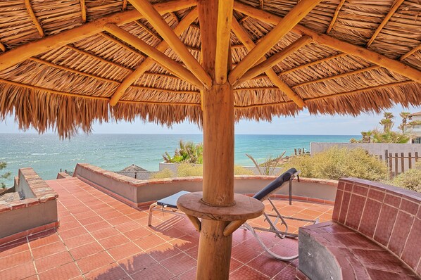 A thatched-roof outdoor area with a view of the sea, a wooden pole, and a bench.