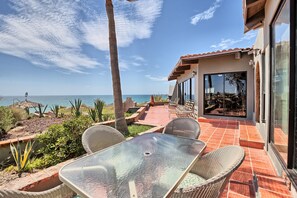 A patio with a glass table and wicker chairs, overlooking a coastal view.