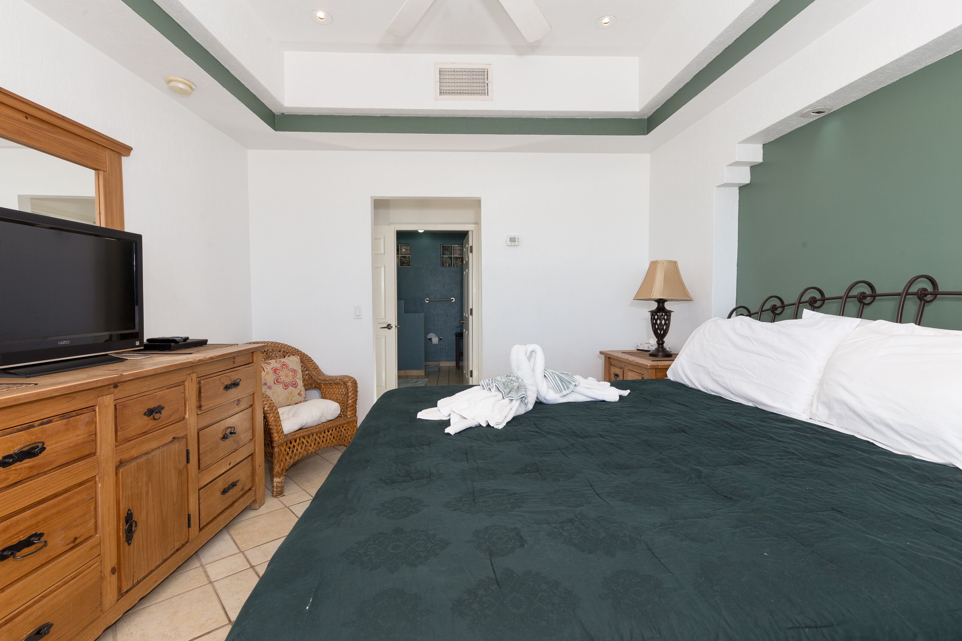 Une chambre à coucher avec un lit, un téléviseur posé sur une commode en bois, une lampe et une porte donnant sur une autre pièce.