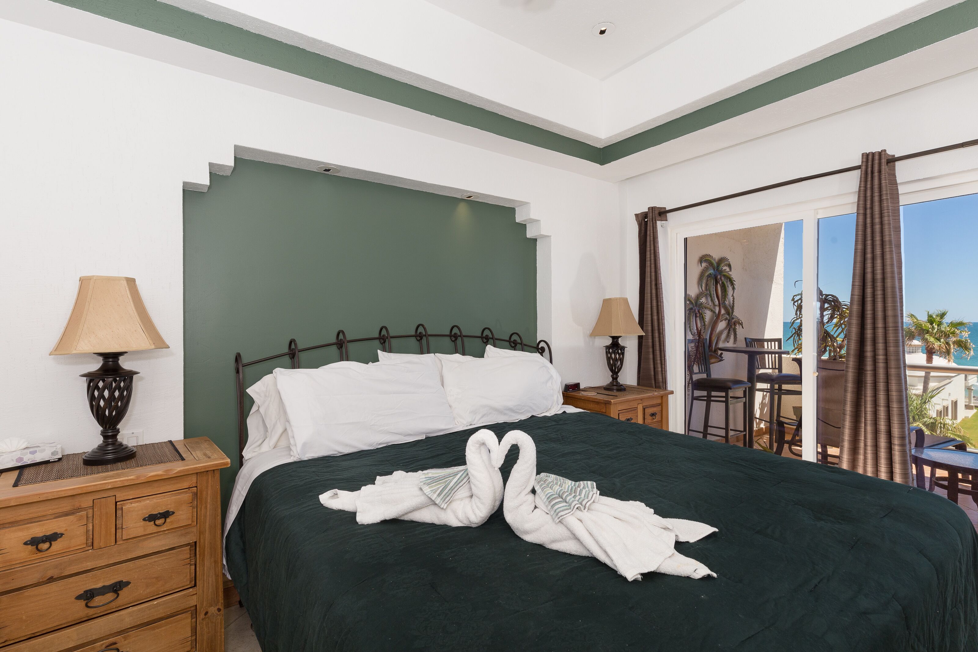 A hotel room with a bed, two nightstands, a dresser, and a balcony with a table and chairs.