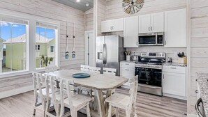 A modern kitchen with white cabinetry, stainless steel appliances, and a wooden dining table. - 114 Seven Palms, Sunshine and Flip Flops (Fulton)