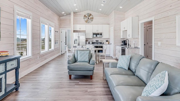 A spacious living area with a sofa, armchair, and dining table, connected to a kitchen and dining area with large windows. - 114 Seven Palms, Sunshine and Flip Flops (Fulton)