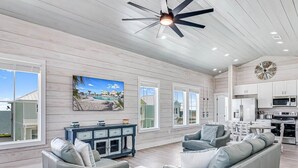 A spacious living room with a ceiling fan, a large window, and a view of the ocean. - 114 Seven Palms, Sunshine and Flip Flops (Fulton)