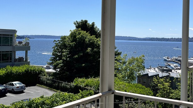 A view of a waterfront property with a clear blue sky, a marina with boats, and a parking area with cars. - Lakeview condo steps to famous Lake Street, Kirkland (Kirkland)