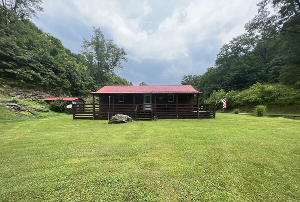 A wooden cabin with a red roof, surrounded by a well-maintained lawn and dense forest.
