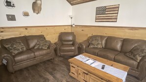 A room with two leather sofas, a wooden coffee table, a wooden ceiling, and a wall with a mounted deer head and an American flag. - Quiet cabin in the hills close to the trails and other outdoor activities.<br> (Genoa)