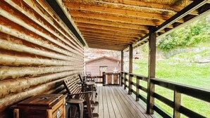 A covered wooden deck with a rustic bench and table, overlooking a grassy area. - Quiet cabin in the hills close to the trails and other outdoor activities.<br> (Genoa)
