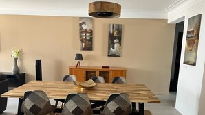 A dining area with a wooden table, four chairs, a vase of flowers, and artwork on the walls. - Appartement Praia Center (PRAIA)