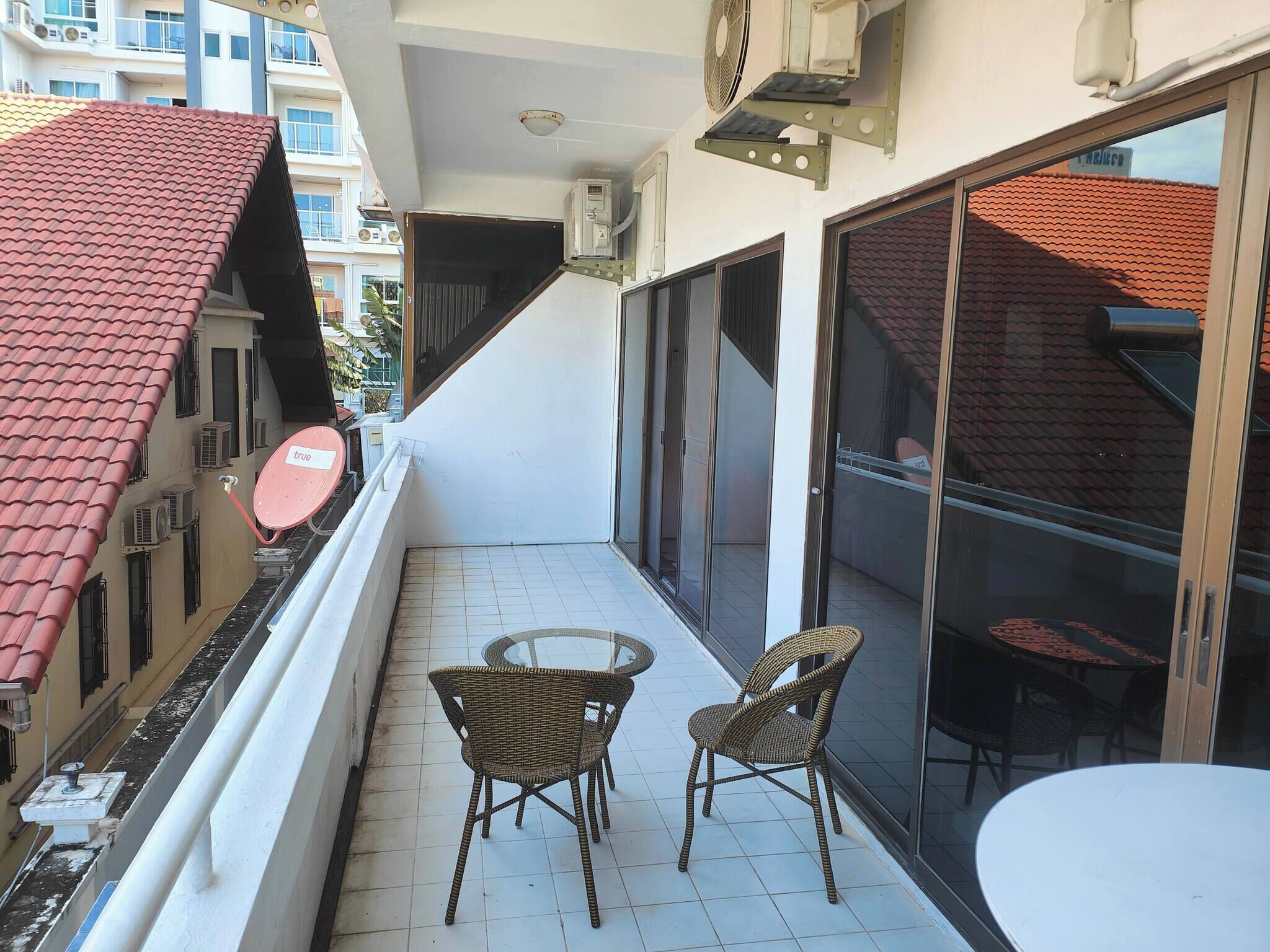 A balcony with two wicker chairs and a small table, overlooking a red-tiled building.