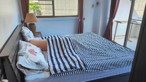 A single bed with striped bedding, a bedside lamp, and a window with curtains. - Big Appartment 101 80 Sqm (Pattaya)