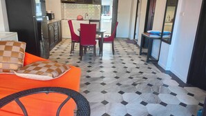 A compact kitchen with dark cabinets, a refrigerator, and a dining area with red chairs. - Big Appartment 101 80 Sqm (Pattaya)