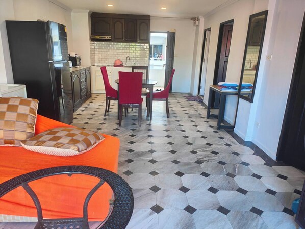A compact kitchen with dark cabinets, a refrigerator, and a dining area with red chairs.