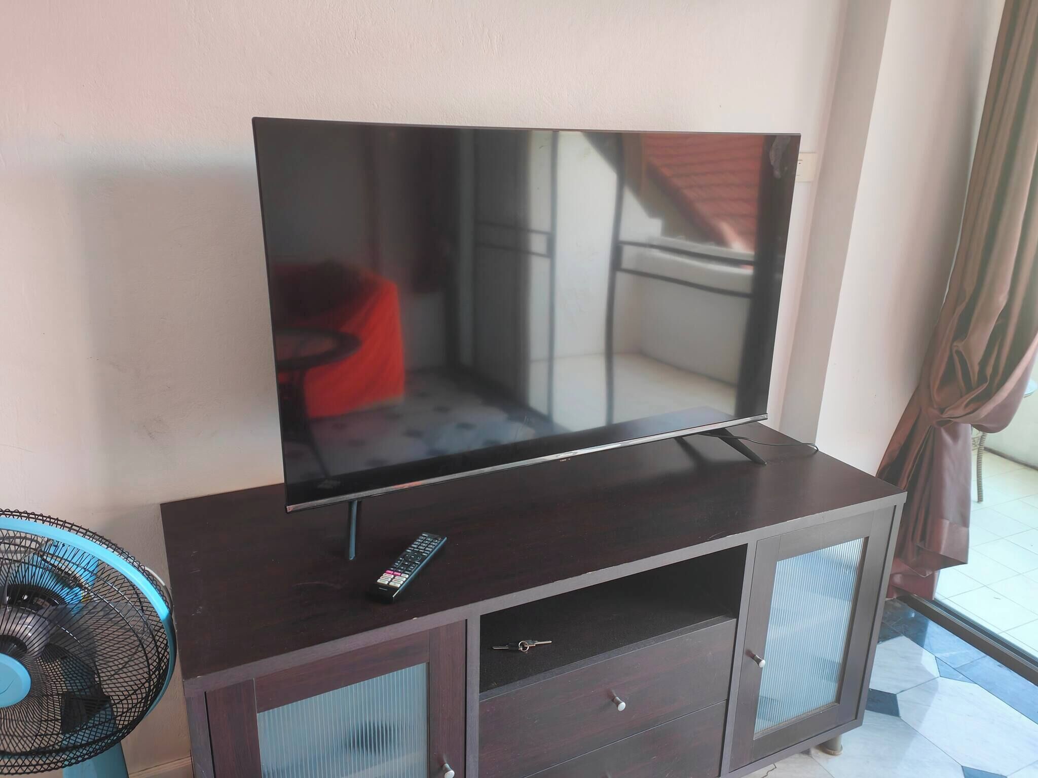 Ein Flachbildfernseher auf einer dunklen Holzkommode, mit einer Fernbedienung darauf.