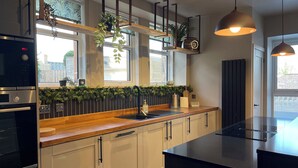 A modern kitchen with a wooden countertop, stainless steel appliances, and pendant lighting.
