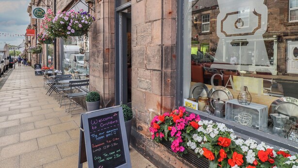 A coffee shop with outdoor seating, a chalkboard menu, and hanging flower baskets.