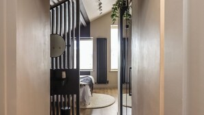 A narrow hallway leading to a bedroom with a bed, a small table, and a potted plant.