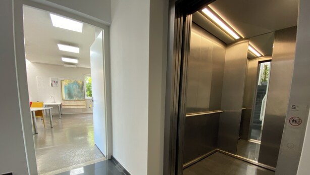 A modern elevator with a metallic interior and a glass door. - Living in a studio - Living in a Studio (Mülheim an der Ruhr)