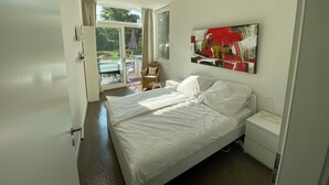 A bedroom with a bed, a nightstand, a wall-mounted abstract painting, and a sliding glass door leading to a balcony. - Living in a studio - Living in a Studio (Mülheim an der Ruhr)
