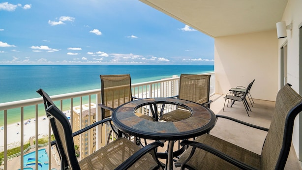 Een balkon met een ronde tafel en stoelen, met uitzicht op een strand en de oceaan.