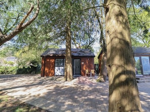 Une petite cabane en bois, surmontée d’un toit en métal, entourée d’arbres et bordée d’un chemin pavé.