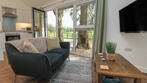 Ein modernes Wohnzimmer mit einer schwarzen Couch, einem Holztisch und einem großen Fenster mit Blick auf einen Baum und einen Zaun.