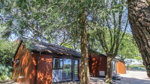 Eine kleine Holzhütte mit Metalldach, umgeben von Bäumen und einer gepflasterten Fläche.