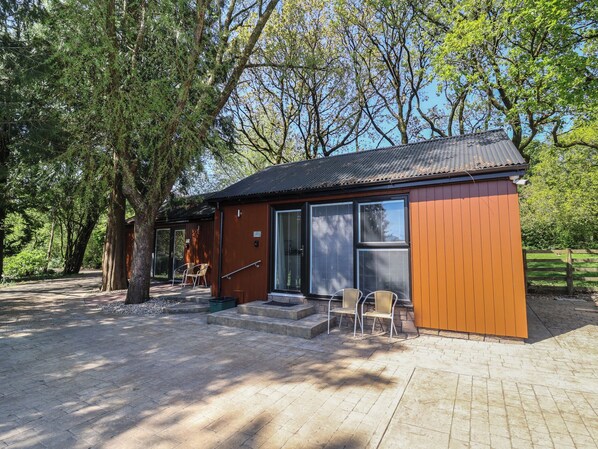 A small wooden cabin with a porch, two chairs, and a staircase leading to the entrance. - Jasmine (Barnstaple)