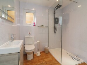 A modern bathroom with a glass-enclosed shower, a white toilet, a sink, and a window above the toilet. - Jasmine (Barnstaple)