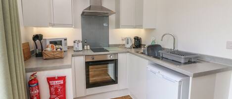 A compact kitchen with white cabinets, a built-in oven, a microwave, a kettle, and a coffee maker.