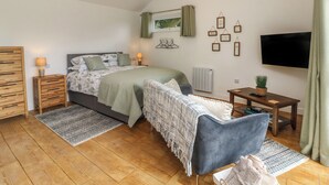 Ein Schlafzimmer mit einem Bett, Nachttischen, einem Fernseher, einem kleinen Tisch mit Pflanze und einem Fenster mit Vorhängen.