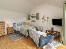 Un dormitorio con una cama, mesitas de noche, un televisor, una pequeña mesa con una planta y una ventana con cortinas.