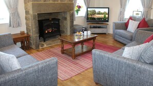A living room with grey sofas, a stone fireplace, a television, and a coffee table. - Jacobswell House – Dog‑Friendly 3‑Bedroom Cottage with Field Views & Cycle Storage (Cramlington)