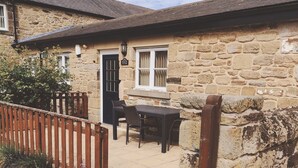A stone cottage with a tiled patio, a wooden fence, and a black door. - Swallow Cottage - Accessible cottage with wetroom, dog friendly, working farm (Cramlington)
