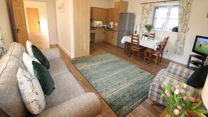 A cozy living room with a sofa, a dining table, and a kitchen in the background. - Swallow Cottage - Accessible cottage with wetroom, dog friendly, working farm (Cramlington)