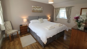 Een slaapkamer met een groot bed, nachtlampjes, een stoel, een nachtkastje, een raam met gordijnen en een schilderij aan de muur.